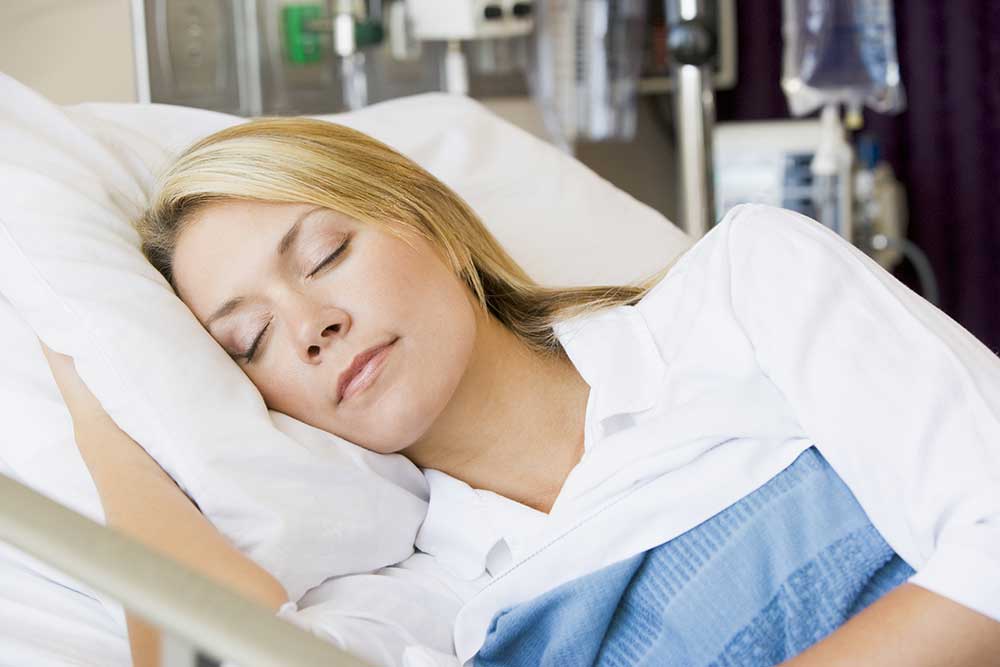 A woman in her medical bed sleeping with her hand under her pillow for support